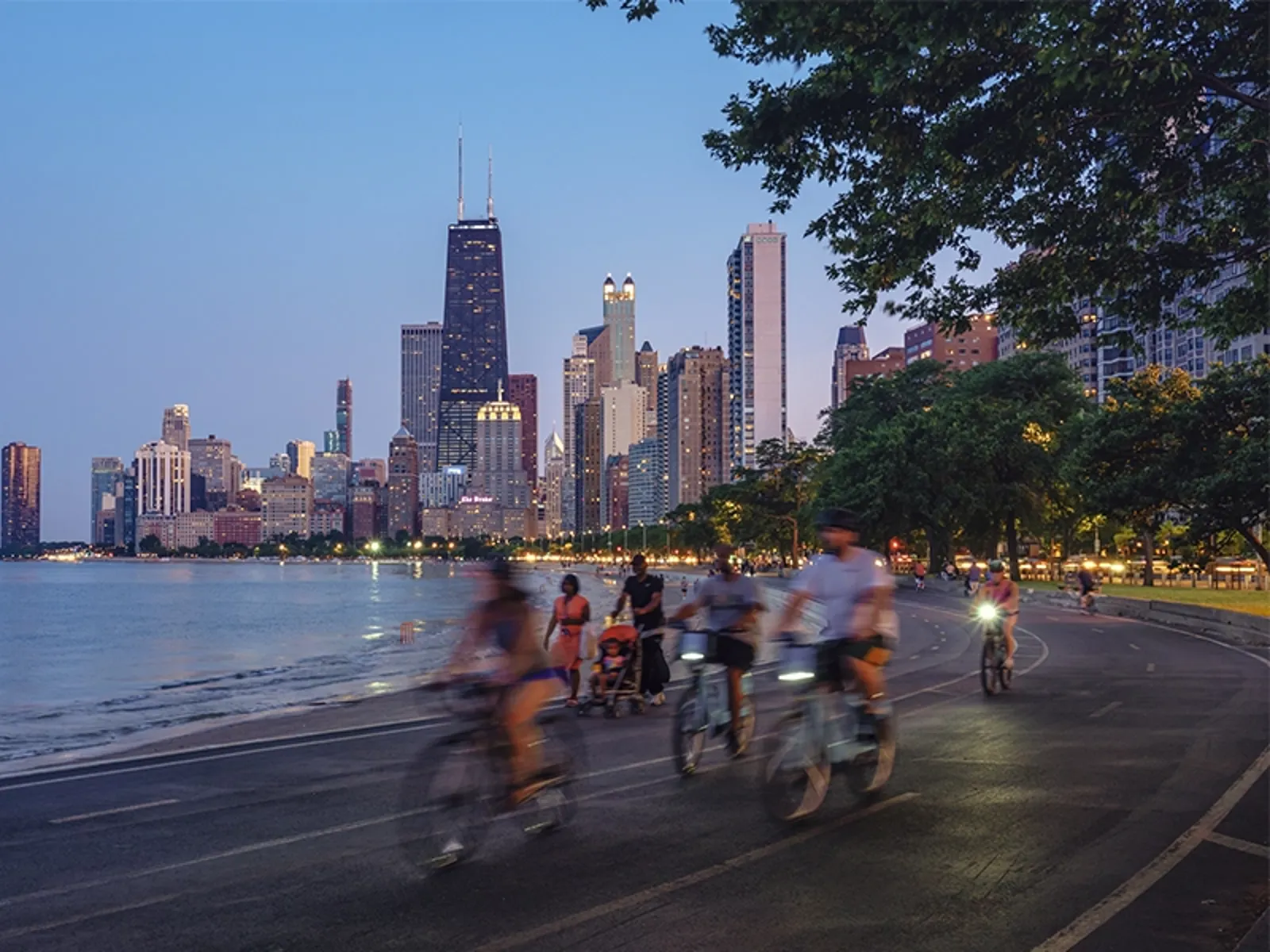 A group of people cycling on a street by a body of water in a city